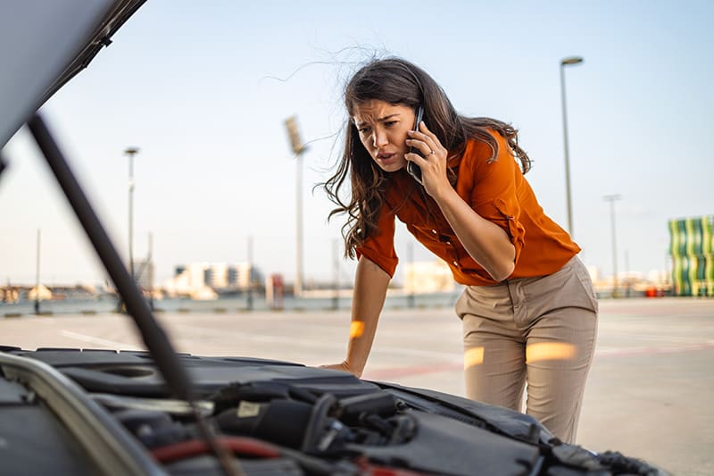 Women making phone call to mechanic looking under the hood of a broken down car-1712730481 Women making phone call to mechanic looking under the hood of a broken down car